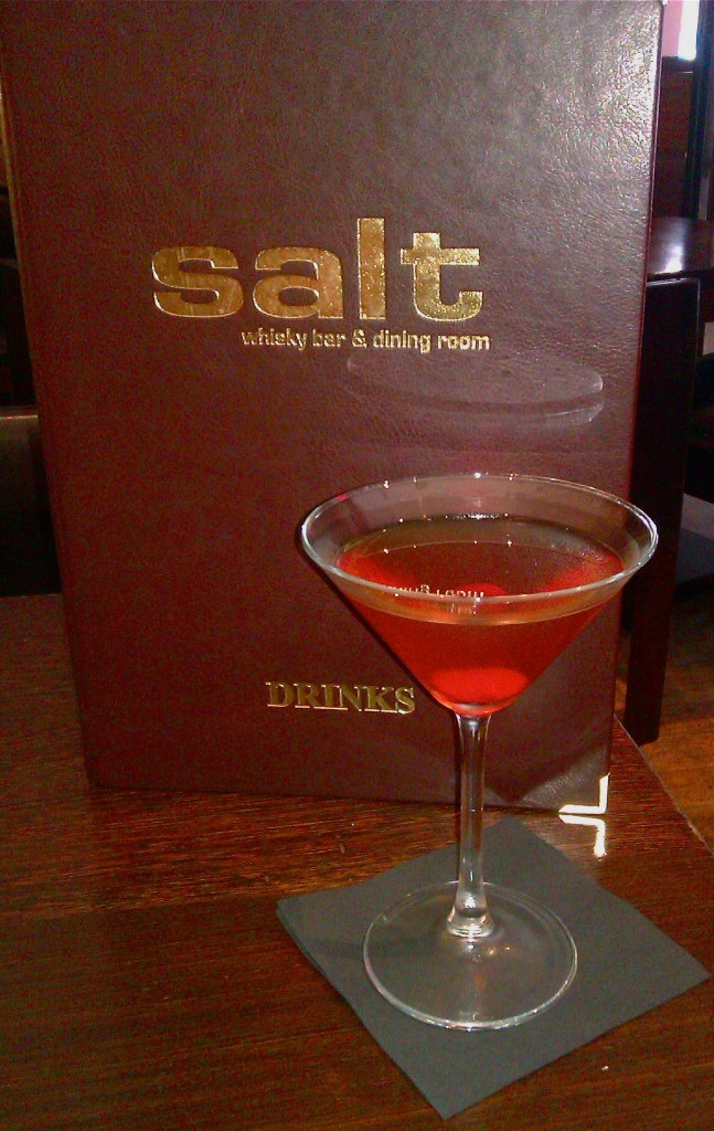 A whisky cocktail in a martini glass sits in front of the menu at Salt Bar